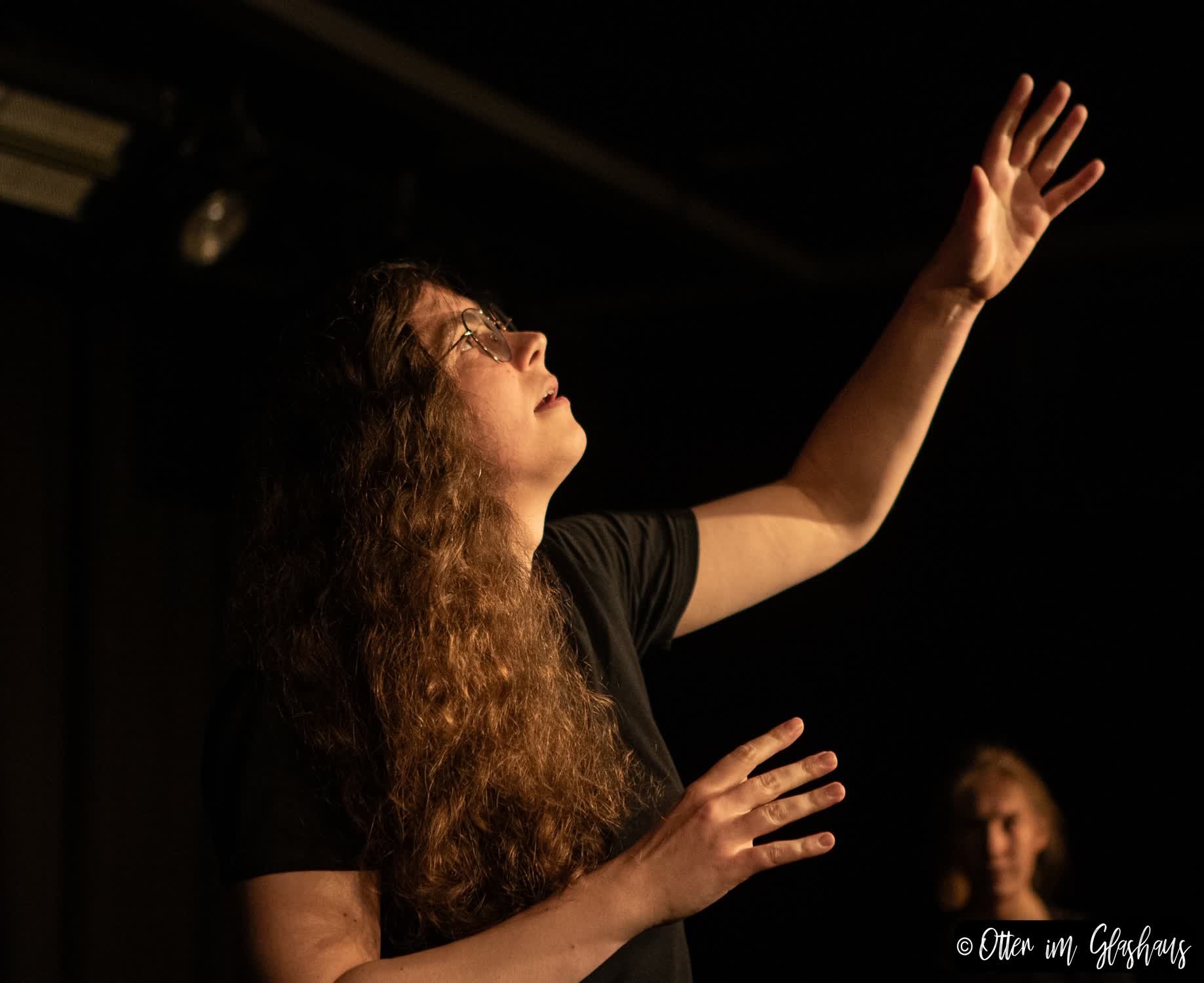 Eine Schauspielerin im Profil. Sie schaut voll Wunder nach oben und streckt ihre Hände dem Himmel entgegen.